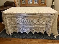 Full tablecloth on a table showing the detailed crochet pattern and scalloped edges.