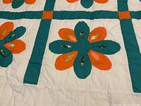 Close-up of quilt with orange and green flower petals on white background, showing hand and machine stitched details.