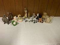 Wide view of the entire group of cat figurines and decor including stone, glass, pewter, and ceramic pieces.