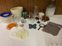 Full view of the lot showing all various decorative items, glass vases, figurines, fabric pieces and small household objects.