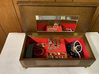 Open wooden jewelry box showing red felt compartments, mirror, and assorted jewelry inside.