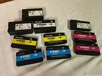 Top-down image of ten HP ink cartridges arranged on a cloth surface; includes multiple black, cyan, yellow, and magenta 950XL and 951XL cartridges.