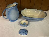 Photo of the full set showing pitcher, bowl, soap dish, and soap dish lid on a white cloth with wood panel background.