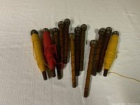 Set of 12 wooden spools laid out on white fabric showing metal capped tops and thread on some spools