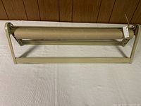 Full view of vintage metal free-standing wrapping paper dispenser holding a roll of kraft paper. Shows frame, rod, and cutter bar.