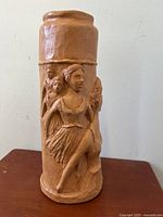 Front view of tall cylindrical terra cotta vase with three-dimensional ballerina dancer sculptures around the body.