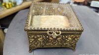 Front angled view of the antique beveled glass gilt metal footed jewelry box, showing intricate gilt metalwork and clear beveled glass panels.