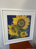 Framed giclee print artwork showing three sunflowers on blue background, signed and numbered by Helen Lucas.