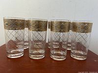 Set of 8 vintage Culver Glass highball drinking glasses arranged in a group with gold gilt etched wide decorative bands and etched cross diamond pattern.