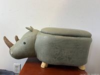 Side view of rhinoceros-shaped ottoman footstool with green faux leather upholstery, brown fabric horns, wood legs, and hinged lid.