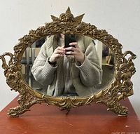 Front view of the ornate Victorian Art Nouveau cast iron tabletop vanity mirror showing kissing cherubs and floral design.