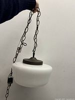 Vintage ceiling lamp with white milk glass shade, metal chain, and canopy, held hanging by a hand showing size and wiring plug.