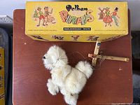 Photo showing white poodle puppet alongside yellow Pelham Puppets box with colorful graphics and illustrations, box measures 12.75 inches long.