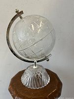 Side view of the etched crystal glass globe showing the textured continents and metal meridian base stand.