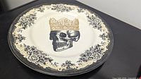 Photo of the round vintage ceramic plate featuring a black skull wearing a gold crown and floral border.