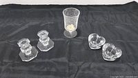 Overview of two Baccarat candle sticks, footed goblet, and two heart-shaped tea light candle holders on black cloth