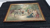 View of lithograph print titled "Forgiven" featuring a historical scene with period dressed men, horses, and a small dog in an outdoor garden setting, visibly framed in wood with gold accents.