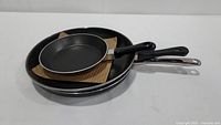 Three fry pans stacked, showing the black non-stick interior and black exterior with metal and plastic handles.