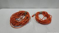 Two coiled orange heavy duty extension cords placed side by side on a white surface. Both appear used but intact.