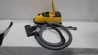 Vacuum body in yellow plastic with grey hose and floor head attached lying on table