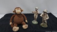 Photo showing plush Spunky Monkey seated next to two metal monkey figurines playing musical instruments on bases.