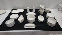 Full set of assorted Pfaltzgraff ivory dishes arranged on a black cloth, showing multiple bowls, plates, mugs, and serving dishes.
