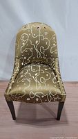 Front view of the slipper style accent chair showing gold silk fabric with abstract embroidery and curved backrest.