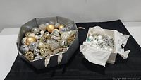 Wide shot showing the large silver and gold Christmas wreath and open box of Christmas balls on a black cloth