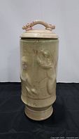 Full view of tall pottery vase showing overall shape, lid with handle, glazing, and some 3D animal-like embellishments on shaft.