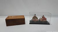 Overall image showing the pair of Emperor and Empress Hina dolls inside a clear display case, next to the original wooden storage box.