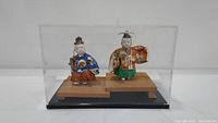 Pair of Hakata dolls in a clear acrylic protective case with wooden platform; dolls visible from front and side