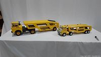 Wide shot showing both large and smaller vintage Tonka yellow steel car carriers on white background with lighter for scale