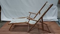 Side view of the vintage wooden deck chair showing its extended footrest and armrests, with striped beige and white fabric.