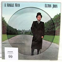 Front cover of Elton John A Single Man picture disc vinyl LP album showing Elton John standing on a pathway, wearing a top hat and coat.