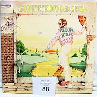 Front cover of the Elton John Goodbye Yellow Brick Road double vinyl LP album featuring Elton John walking on a yellow brick road illustration.