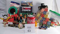 Photo showing assortment of vintage toys and games including character figurines, wooden blocks, toy vehicles, and boxed games arranged on white background.