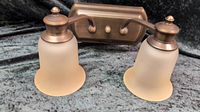 Bronze finished 2 light bath bar with cream frosted glass shades on bell shaped fixtures.