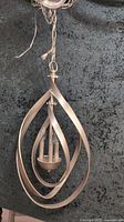 Photo of one gold-silver finish 3 light pendant with overlapping swirl metal frames hanging, showing vertical bulbs inside.