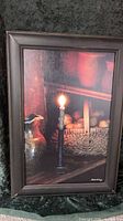 Photo of framed print showing a lit candle on a rustic shelf with kitchen items including a ceramic jug and basket of onions.