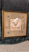 Front of framed picture showing rooster motif with star corner details.