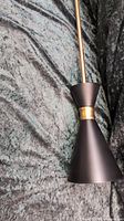 Side view showing black conical pendant shade with central gold band, laid on black crushed velvet fabric.