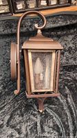 Side view of the dark bronze outdoor wall sconce with curved arm and lantern-style light holder.