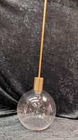 Full view of the pendant light hanging vertically showing the entire glass globe and rod suspension with brushed gold metal top.