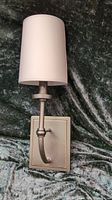 Front view of bronze wall sconce showing rectangular backplate, curved arm, and white fabric cylindrical lampshade.