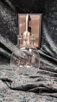 Photo of a single brushed nickel and black wall sconce with clear glass shade against black fabric background