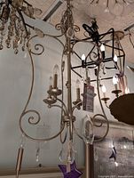 Silver gold chandelier with ornate scrollwork and hanging glass accents, photographed hanging from the ceiling among other light fixtures.