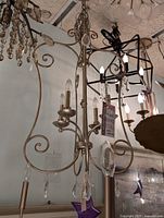 Photo of a decorative chandelier with silver gold toned metal and glass accents, showing candle-style light fixtures and hanging glass pieces.