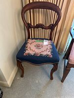Full front view of the antique balloon back chair showing wood frame and needlepoint seat upholstery with floral design.