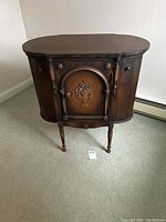 Full front view of oval-top wooden sewing cabinet showing spindled legs and front door.