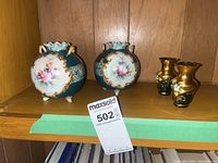 Shelf display of two antique round porcelain vases with floral hand painted designs and two small green glass floral vases.
